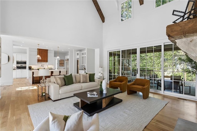 living room with beamed ceiling, a towering ceiling, and light hardwood / wood-style flooring