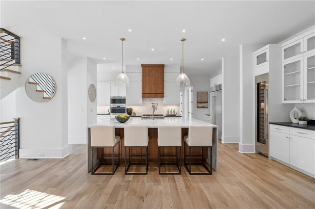 kitchen with a center island with sink, white cabinets, and decorative light fixtures