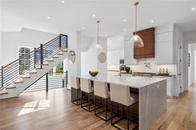 kitchen with white cabinets, decorative light fixtures, light hardwood / wood-style floors, and an island with sink