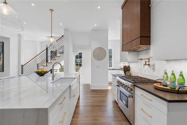 kitchen with white cabinets, hanging light fixtures, stainless steel stove, and an island with sink