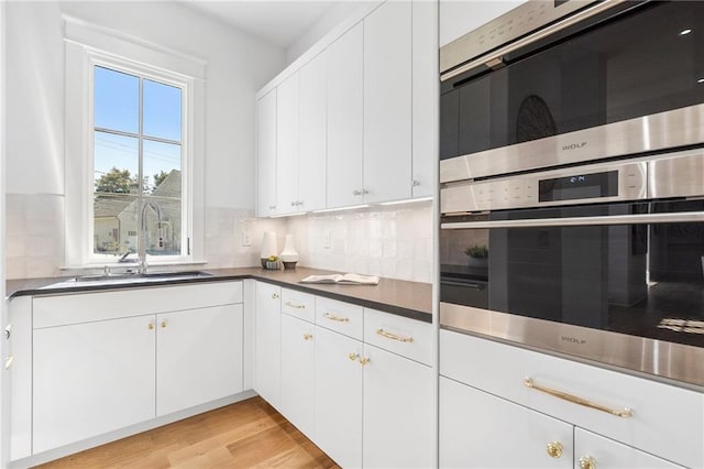 kitchen with white cabinets, light hardwood / wood-style flooring, sink, and tasteful backsplash