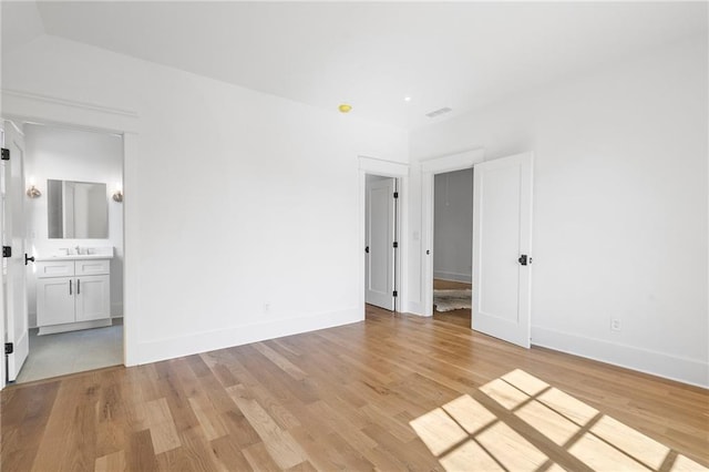 unfurnished bedroom featuring connected bathroom, sink, and light hardwood / wood-style floors