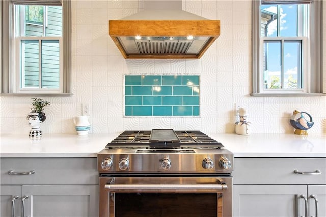 kitchen featuring gray cabinets, wall chimney exhaust hood, backsplash, and stainless steel stove