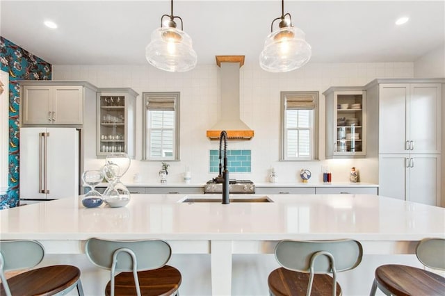 kitchen with high end white refrigerator, hanging light fixtures, gray cabinetry, and wall chimney range hood