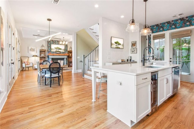 kitchen featuring white cabinetry, sink, beverage cooler, an island with sink, and decorative light fixtures