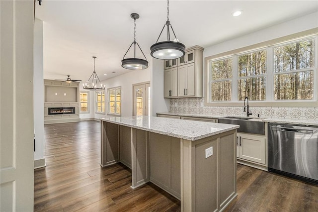 kitchen with sink, light stone counters, stainless steel dishwasher, a kitchen island, and pendant lighting