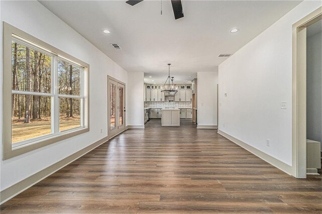 unfurnished living room with ceiling fan with notable chandelier and dark hardwood / wood-style floors