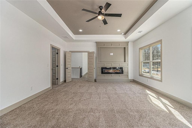 unfurnished living room featuring ceiling fan, carpet floors, a fireplace, and a tray ceiling