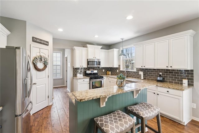 kitchen featuring pendant lighting, a breakfast bar, appliances with stainless steel finishes, white cabinetry, and hardwood / wood-style floors