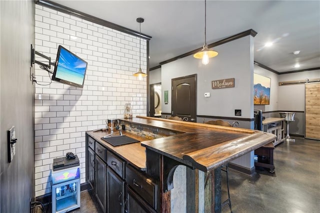 kitchen with butcher block countertops, a kitchen bar, hanging light fixtures, ornamental molding, and a barn door