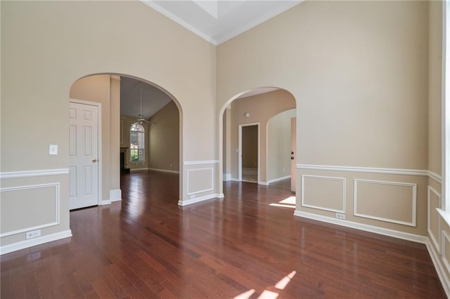 spare room featuring baseboards, arched walkways, ornamental molding, a towering ceiling, and wood finished floors