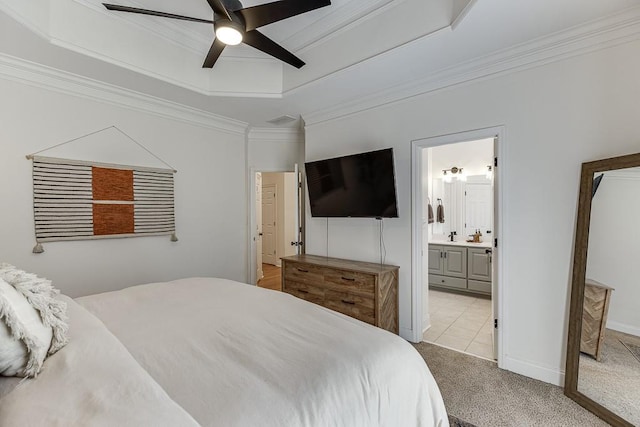 carpeted bedroom featuring a raised ceiling, ornamental molding, a ceiling fan, ensuite bath, and baseboards