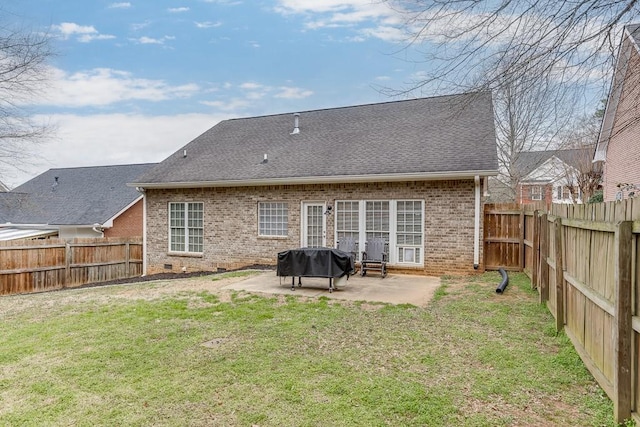 back of property featuring brick siding, a yard, a shingled roof, a patio area, and a fenced backyard