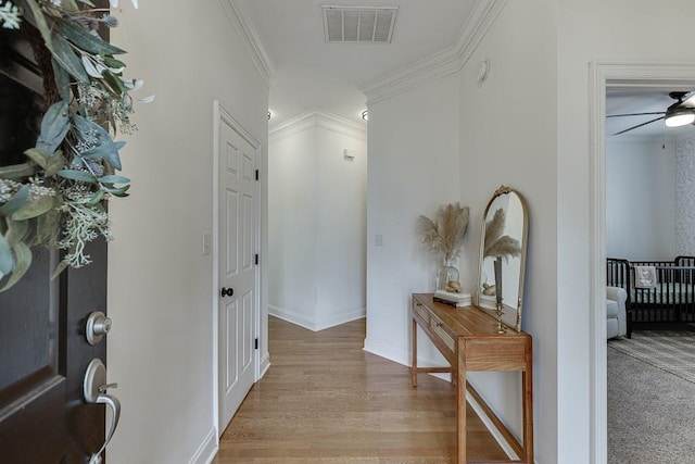 corridor featuring baseboards, light wood-style floors, visible vents, and crown molding