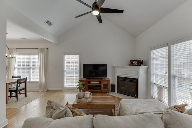 living room featuring ceiling fan with notable chandelier, light wood finished floors, a fireplace with flush hearth, and visible vents