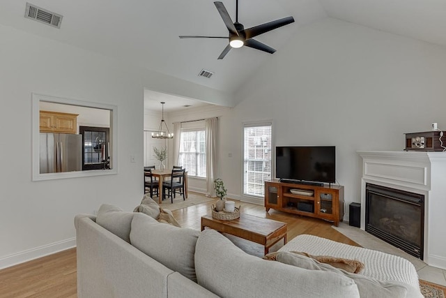 living room featuring light wood-style floors, a glass covered fireplace, visible vents, and ceiling fan with notable chandelier