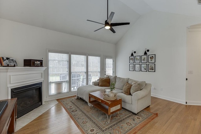 living area featuring light wood-style flooring, baseboards, a ceiling fan, and a tile fireplace