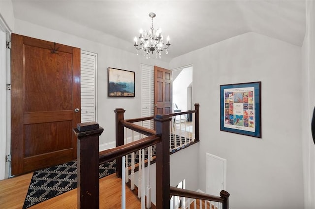 hallway featuring an upstairs landing, light wood finished floors, a notable chandelier, and lofted ceiling