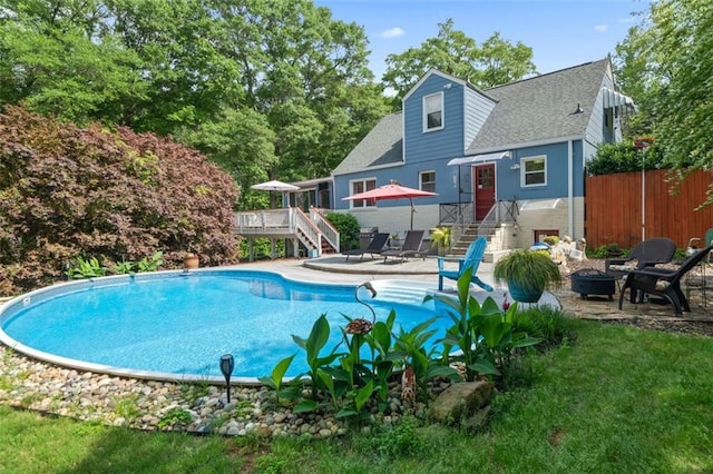 pool with a wooden deck, a patio area, an outdoor fire pit, fence, and stairway
