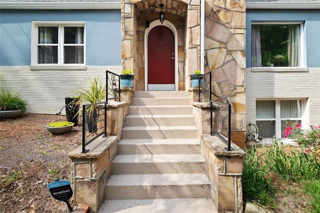 property entrance featuring stucco siding, a shingled roof, and stone siding