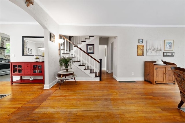 foyer with light wood finished floors, stairs, baseboards, ornamental molding, and arched walkways