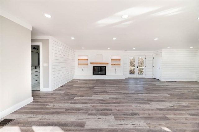 unfurnished living room featuring french doors, recessed lighting, visible vents, a glass covered fireplace, and wood finished floors