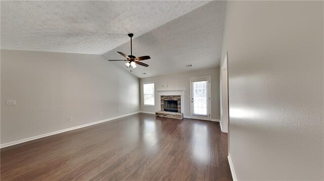 unfurnished living room with ceiling fan, a textured ceiling, dark wood-style flooring, and a stone fireplace