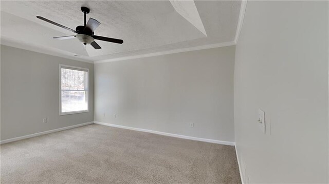 spare room with a tray ceiling, crown molding, light colored carpet, a ceiling fan, and baseboards