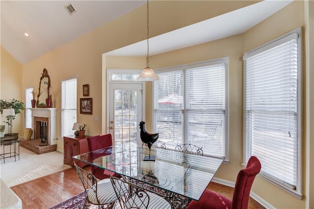 dining space featuring a brick fireplace, hardwood / wood-style floors, a healthy amount of sunlight, and vaulted ceiling