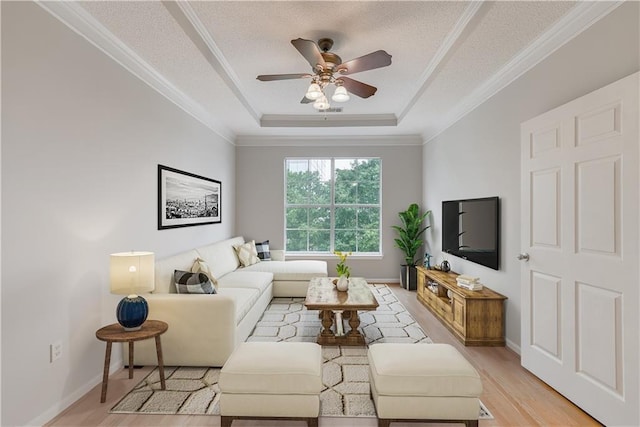 living room with ornamental molding, a textured ceiling, a raised ceiling, ceiling fan, and light hardwood / wood-style floors