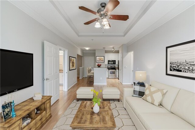 living room featuring ceiling fan, light hardwood / wood-style floors, a raised ceiling, and crown molding