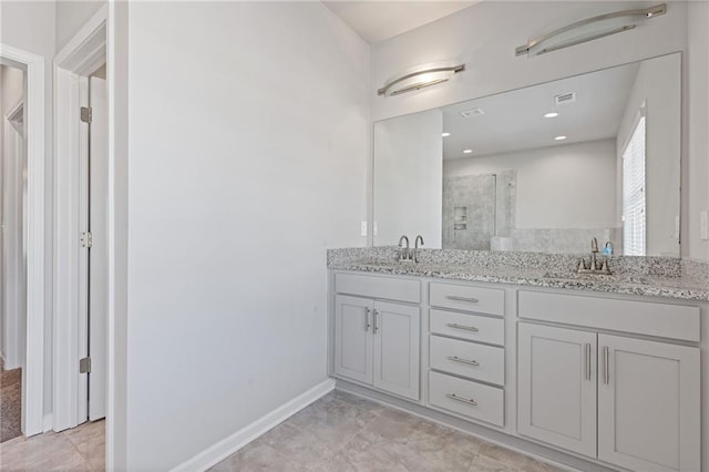 full bath with double vanity, a shower stall, baseboards, and a sink