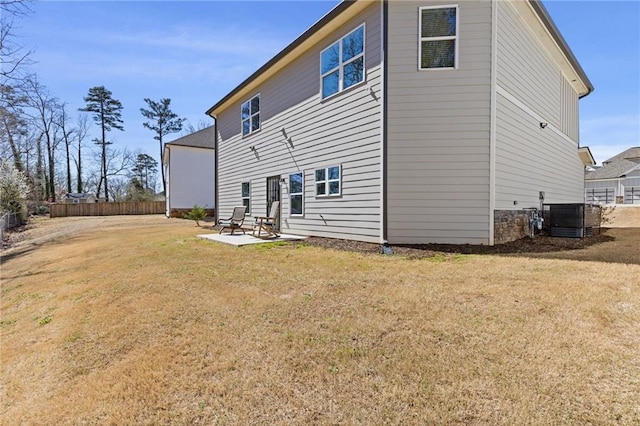 back of property with fence, central AC unit, a yard, stone siding, and a patio