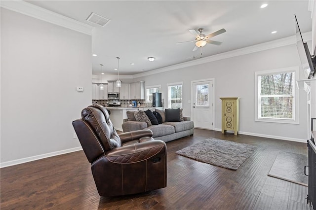 living room featuring dark wood-type flooring, visible vents, a wealth of natural light, and ornamental molding