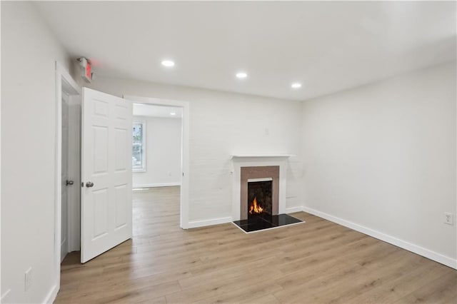 unfurnished living room featuring recessed lighting, baseboards, light wood-type flooring, and a warm lit fireplace