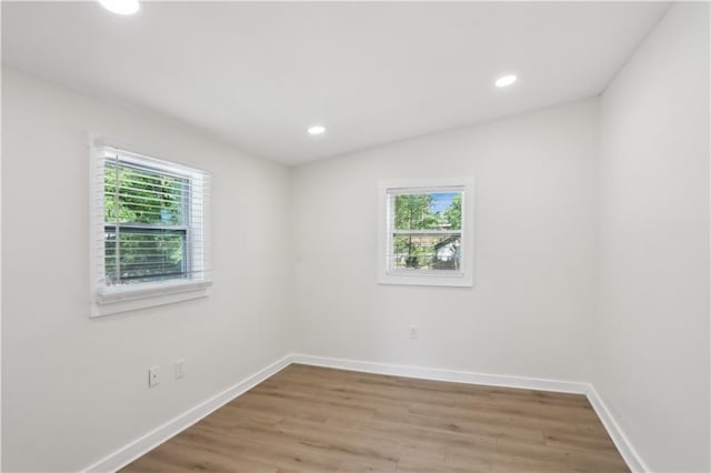 unfurnished room featuring baseboards, recessed lighting, wood finished floors, and a wealth of natural light