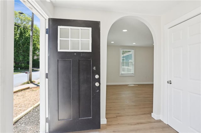 foyer with a healthy amount of sunlight, arched walkways, baseboards, and wood finished floors