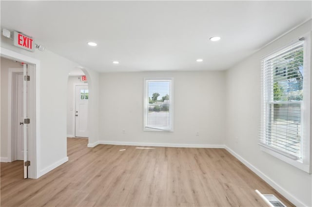 empty room with arched walkways, baseboards, plenty of natural light, and light wood-style floors