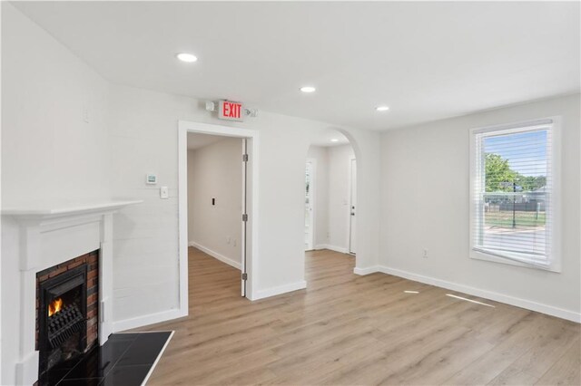 unfurnished living room with arched walkways, baseboards, a lit fireplace, and light wood finished floors
