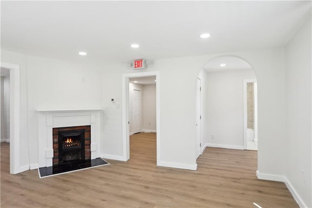unfurnished living room with a fireplace, arched walkways, recessed lighting, baseboards, and light wood-type flooring