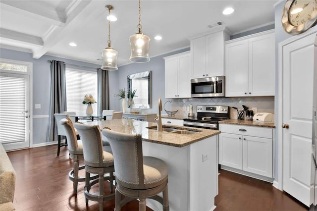 kitchen with appliances with stainless steel finishes, white cabinets, dark stone countertops, beam ceiling, and an island with sink