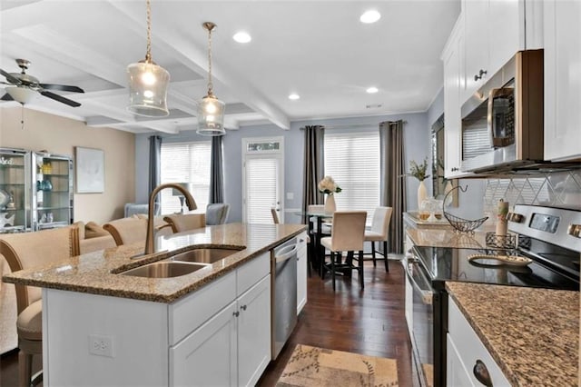 kitchen featuring white cabinets, decorative light fixtures, stainless steel appliances, sink, and a center island with sink