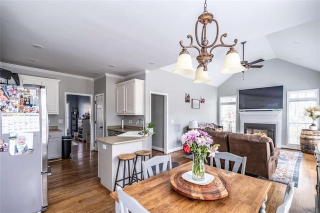 dining area with dark wood-type flooring, an inviting chandelier, sink, vaulted ceiling, and ornamental molding