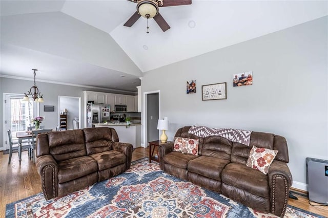 living room with ceiling fan with notable chandelier, light wood-type flooring, and lofted ceiling