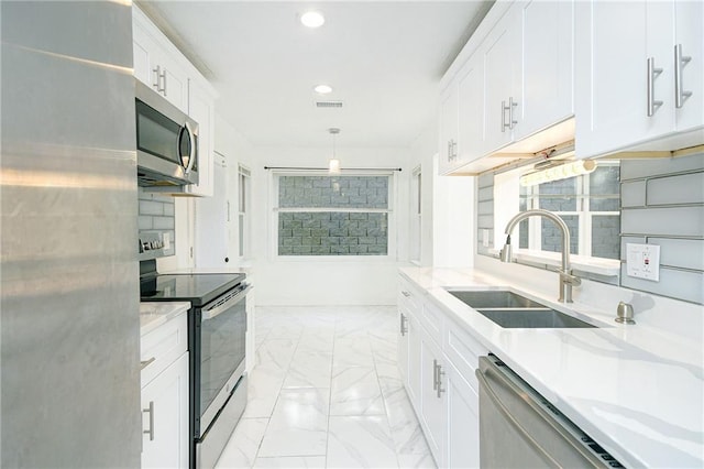 kitchen with sink, white cabinetry, pendant lighting, stainless steel appliances, and light stone countertops