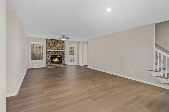 unfurnished living room with a stone fireplace, wood-type flooring, and ceiling fan