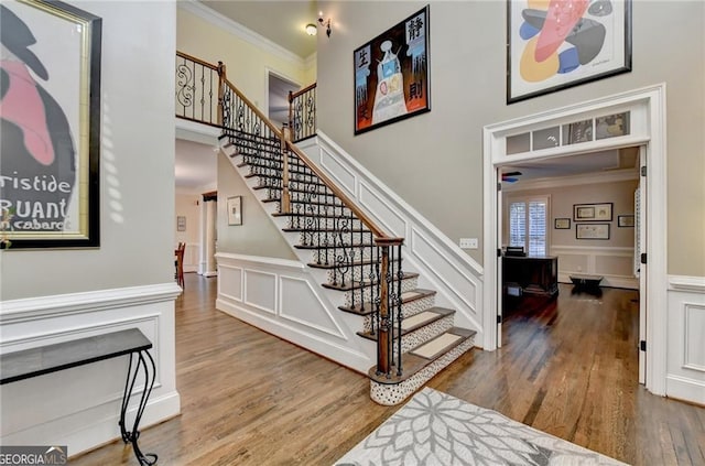 stairs featuring a towering ceiling, wood finished floors, crown molding, and a decorative wall