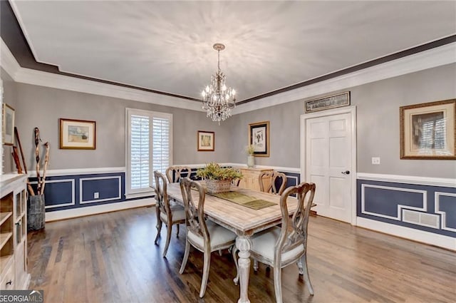 dining area with wood finished floors, ornamental molding, wainscoting, and a notable chandelier