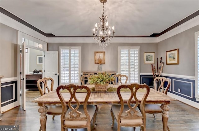 dining area with a wainscoted wall, wood finished floors, a notable chandelier, and crown molding
