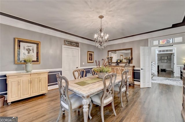 dining room featuring ornamental molding, a decorative wall, wood finished floors, and a chandelier